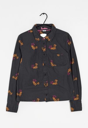 Chemise boutonnée gris foncé à manches longues, décorée de teckels orange portant des couronnes roses, suspendue sur un cintre noir.
