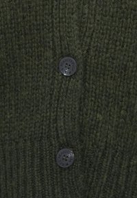 Cardigan tricotat de culoare verde închis, cu un model texturat, având două nasturi negri cu inscripția "Marc O'Polo" pentru închidere.