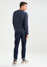 Maglione a maniche lunghe in maglia navy abbinato a jeans scuri e scarpe da ginnastica grigie. Il maglione ha un collo a giro e un design aderente.