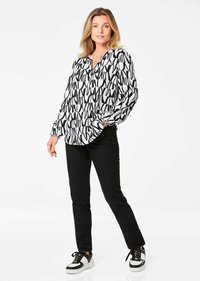 Zwart-wit gemusterde blouse met lange mouwen, een V-hals, een relaxte pasvorm en elastische manchetten, gecombineerd met zwarte slim-fit broek en sneakers.
