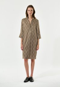 Braun gemustertes Kleid mit dreiviertel Ärmeln, einem Kragen und geradem Schnitt. Kombiniert mit schwarzen Slippern.