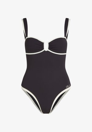 Schwarzer Badeanzug mit weißen Akzenten, ausgestattet mit geformten Körbchen, gerafftem Vorderteil und verstellbaren Trägern. Glatte Stoffstruktur.