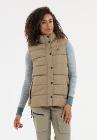 Beige Steppweste mit hohem Kragen, Knopfverschluss und seitlichen Taschen. Wird über einem hellgrauen Langarmoberteil getragen. Strukturierter Stoff mit gestepptem Design.