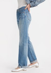 Jeans de mezclilla rectos en azul claro, con cintura de media altura, diseño clásico de cinco bolsillos y un ligero desgaste. Combinados con bailarinas plateadas.