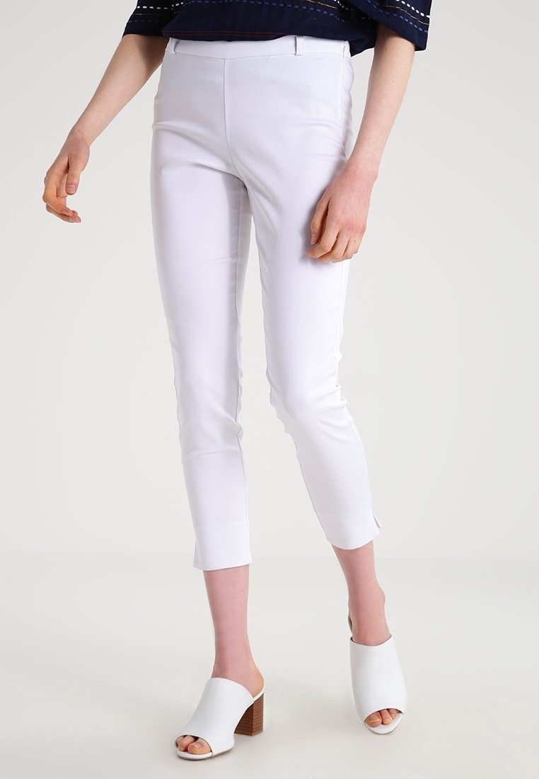 Pantalon blanc ajusté avec un design court. Confectionné dans un tissu lisse, présentant une coupe slim et des ourlets retroussés. Porté avec des mules blanches à bout ouvert.