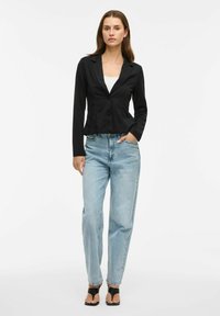 Juodas trumpas švarkas su įpjautu apykakle, ilgomis rankovėmis ir vienu mygtuku, derinamas su šviesiai mėlynomis aukštu liemeniu džinsais.