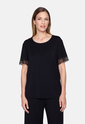 Kvinde med glat, skulderlangt hår iført en sort kortærmet top med blonder på ærmerne mod en ensartet hvid baggrund.