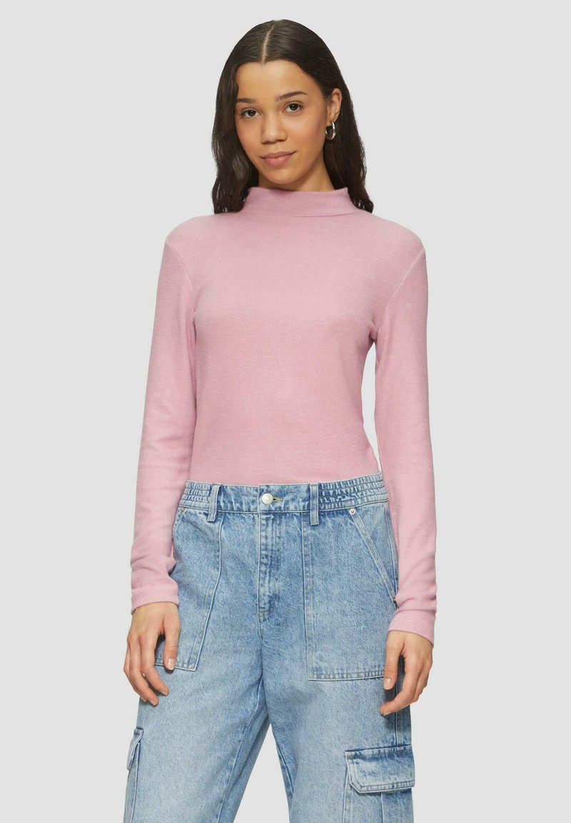 Jasnoróżowa, długosleeve'owa bluzka z wysokim dekoltem, zestawiona z luźnymi niebieskimi spodniami cargo z denimu, które mają kieszenie i teksturowany splot.