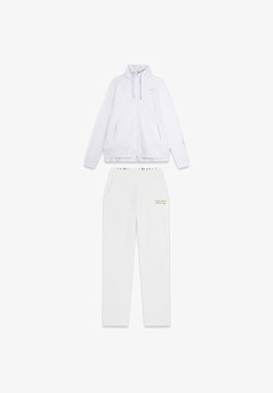 Ensemble de survêtement blanc comprenant une veste zippée avec un col haut et un pantalon assorti. Accents dorés et logo sur les deux pièces. Texture lisse.