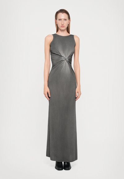 Robe maxi grise sans manches avec un détail noué à la taille, texture lisse et silhouette ajustée, associée à des bottines noires à la cheville.