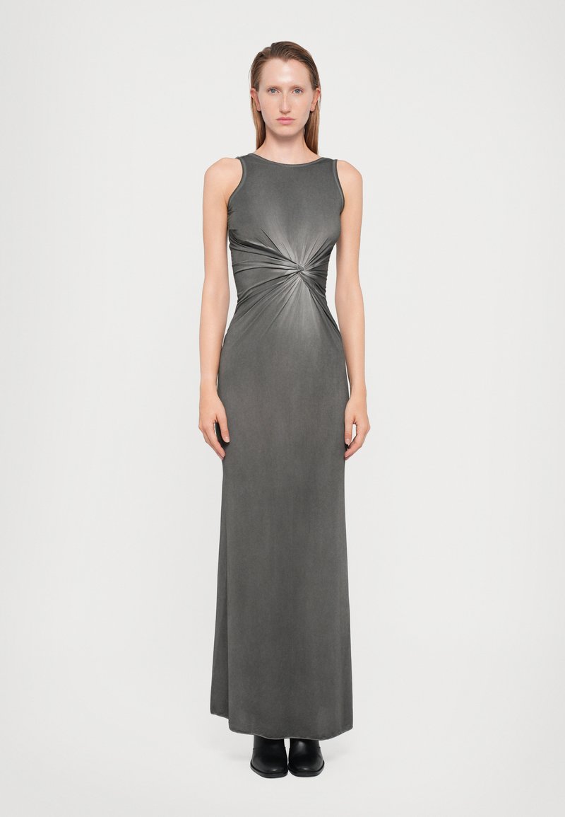 Abito maxi grigio senza maniche con dettaglio a torsione in vita, texture liscia e silhouette aderente, abbinato a stivaletti neri alla caviglia.