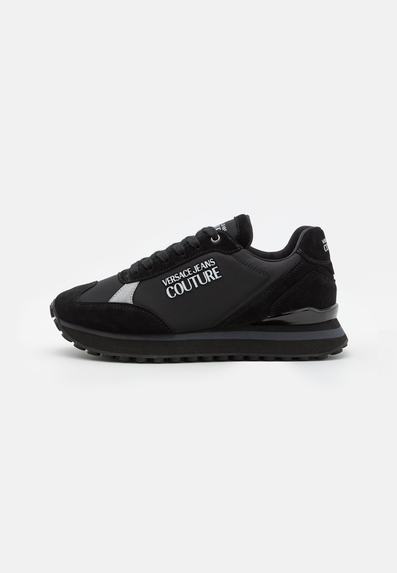 Baskets noires Versace Jeans Couture à lacets, logo blanc sur le côté et semelle texturée visibles de l’extérieur.