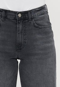Jeans in denim grigio scuro con un design aderente, cinque tasche e chiusura a bottone in vita. Dettaglio di sfumature sottili sul tessuto.
