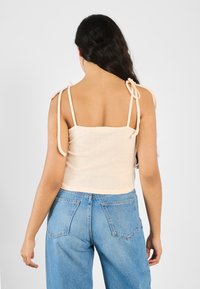 Ferskenfarvet strikket top med tynde bindebånd, tekstureret stof med små huller, parret med højttaljede blå jeans. Bagfra set.