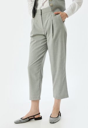 Graue, plissierte Hosen aus strukturiertem Stoff, mit hoher Taille und kurzer Länge, kombiniert mit Slingback-Schuhen, die mit Verzierungen geschmückt sind.