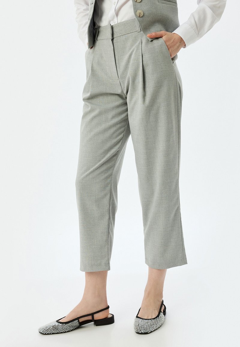 Pantalones plisados grises hechos de una tela texturizada, con cintura alta y longitud recortada, combinados con zapatos de tacón con tira en el talón adornados con embellishments.