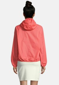 Giacca a vento leggera di colore corallo, con cappuccio, polsini elastici e orlo elastico. La parte posteriore presenta una texture liscia e opaca con un design minimalista.