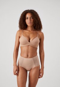 Naadloze draadloze beha in naaktkleur met gladde cups en verstelbare bandjes, gecombineerd met high-waist slip met getextureerde mesh zijpanelen.
