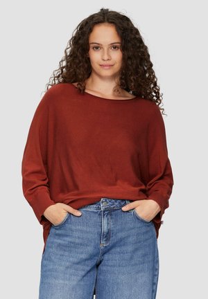 Pull ample couleur rouille avec encolure large et manches longues, associé à un jean bleu taille haute. Tissu doux avec une texture lisse.