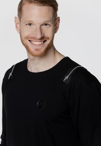 Czarna, długosleeve koszula z srebrnymi zamkami na ramionach, teksturowany materiał i okrągły dekolt. Posiada okrągłe, czarne logo na piersi.