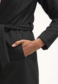 Cappotto avvolgente nero con finitura testurizzata, dotato di cintura, maniche lunghe e tasca laterale, che mette in mostra un design liscio ed elegante.