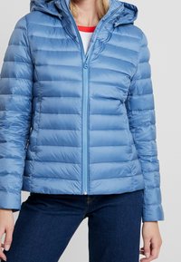 Jasnoniebieska kurtka puchowa z poziomymi przeszyciami, zapinana na zamek z przodu, z regulowanym kapturem, wykonana z gładkiego, lekko błyszczącego materiału.