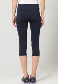 Navyfärgade kortbyxor i stretchmaterial med nätpaneler på vaderna och en slät midja. Bärs med svarta och lila träningsskor.