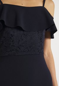 Vestido azul-marinho com um topo franzido e um corpete de renda com padrões florais. Tecido liso abaixo da cintura, exibindo uma silhueta ajustada.