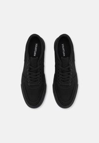 Black canvas shoes with a low profile, lace closures, textured uppers, and branding on the insoles. Rubber outsoles for traction.