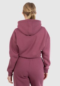 Felpa bordeaux con cappuccio grande, polsini elastici e vestibilità comoda. Tessuto morbido con una texture liscia. Presenta un cordino per la regolazione.
