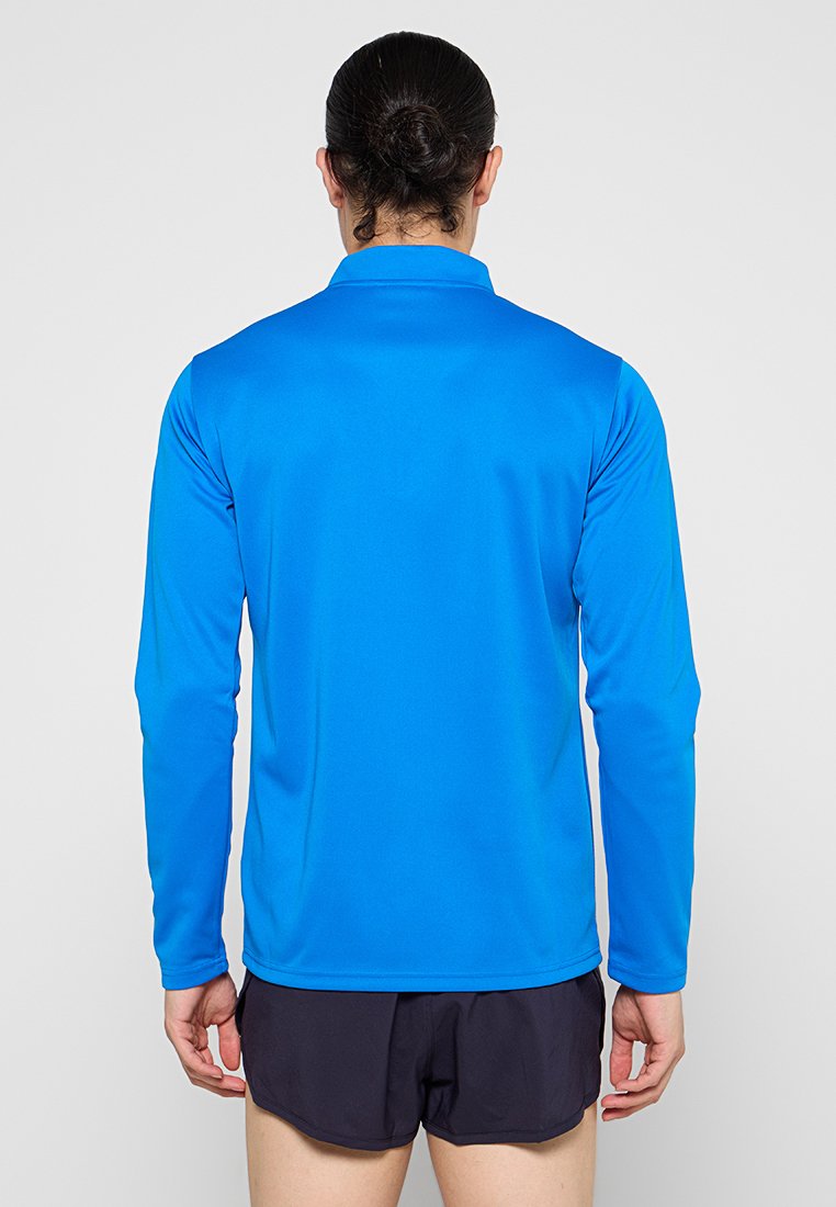 Camisa atlética de manga larga de color azul brillante, hecha de un tejido ligero y suave con cuello; combinada con pantalones cortos oscuros.