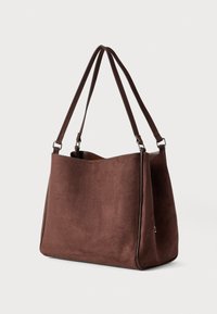 Καφέ τσάντα tote από σουέτ με διπλούς ιμάντες ώμου και ευρύχωρο ανοιχτό πάνω μέρος, πάνω σε απλό φωτισμένο φόντο.
