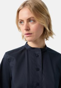 Navy blue shirt with a high collar, front buttons, and a smooth texture. The fabric appears lightweight and slightly glossy.