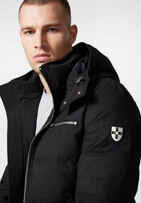 Czarna kurtka puchowa z wyprofilowanym kołnierzem, z przodu na zamek, kieszenią na piersi oraz naszywką z logo na rękawie. Gładki materiał zewnętrzny i izolacja.