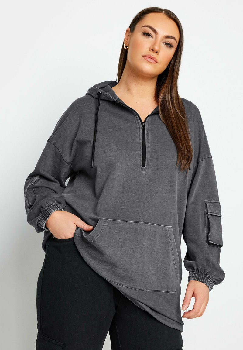 Grå huvtröja med dragkedja i nacken, ribbad struktur, stor framficka och elastiska muddar. Har sidofickor på ärmarna.