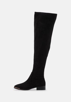 Botte haute jusqu'au genou en daim noir avec talon bas et pointe effilée, semelle plate et texture lisse sur fond blanc uni.