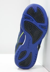 Blauwe sportschoenzool met een gestructureerde zwarte rubberen loopvlak. Geel-groene accenten langs de zijkanten en stevige materiaalkonstruktion.