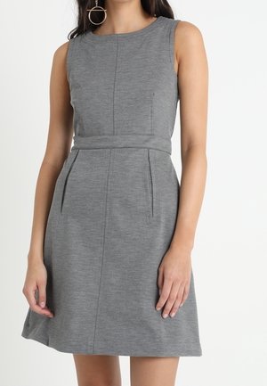 Ærmeløs grå kjole til knæene med bælte i taljen, båret af en person, kombineret med en stor cirkulær hængende ørestik i venstre øre.