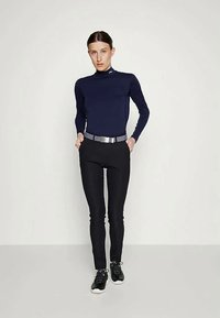 Zelena dolga majica z visokim ovratnikom, v kombinaciji s črnimi oprijetimi hlačami in črnimi športnimi copati. Obleka dopolnjuje srebrni pas.