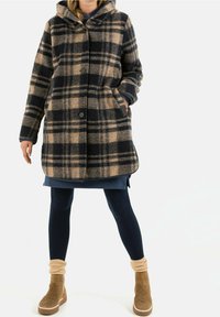 Geverifieerde wollen jas in beige en marineblauw, met capuchon, knopen en zijzakken. Draagt over een blauwe jurk en gecombineerd met tan enkellaarsjes.