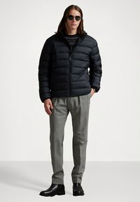 Črno puhasto jakno z vodoravnimi šivi, sprednjim zadrgo in stranskimi žepi. Kombinirana s svetlo sivimi hlačami in črnimi usnjenimi škornji.