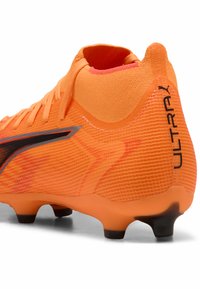 Scarpa da calcio di un vivace arancione con una tomaia in rete testurizzata, caratterizzata da una striscia nera e un design del tallone curvo per una vestibilità ottimale.