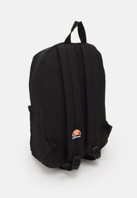Sac à dos noir avec des bretelles rembourrées, deux poches latérales et un patch rond avec un logo présentant des accents rouges, orange et blancs.