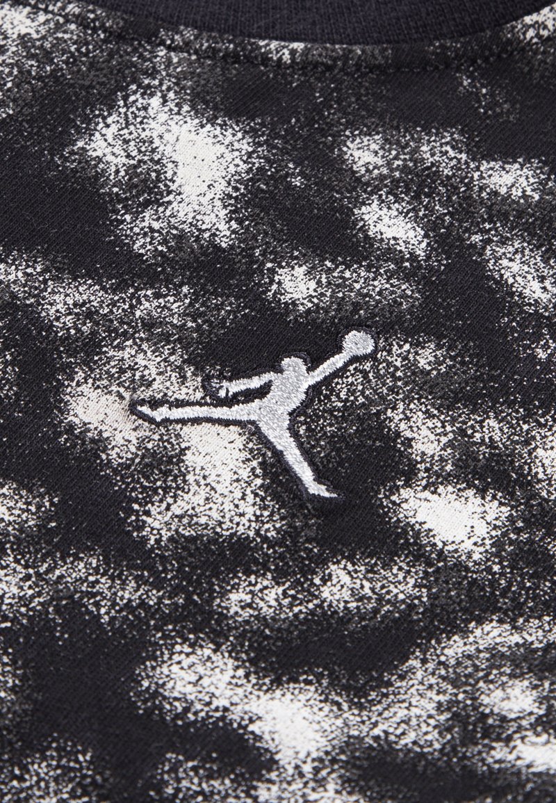 T-shirt in tessuto a tinta unita bianco e nero con un'impressione prominente di una silhouette grigia ricamata di una figura che salta con un pallone da basket.