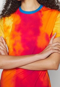 T-shirt à manches courtes avec un motif tie-dye vibrant dans des tons d'orange, rose et jaune, avec un col côtelé bleu.