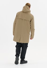 Beige wasserdichte Jacke mit Rückenbelüftung, verstellbarem Kapuze und schwarzen Hosen. Mit elastischen Bündchen und strukturierten Sneaker-Sohlen.