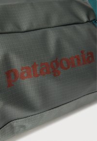 Κοντινό πλάνο γκρι υφασμάτινου υλικού με κόκκινο λογότυπο "patagonia" τυπωμένο πάνω του, μέρος μιας τσάντας ή σακιδίου.