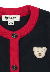 Cardigan per neonati blu navy con colletto e pattina rossi a coste, bottoni neri con etichetta Steiff, e volto di orso bianco ricamato sul petto.