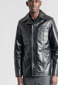 Zwarte leren jas met een grote kraag, voormet knopen en twee borstzakken. Heeft een soepele textuur en een getailleerde pasvorm.