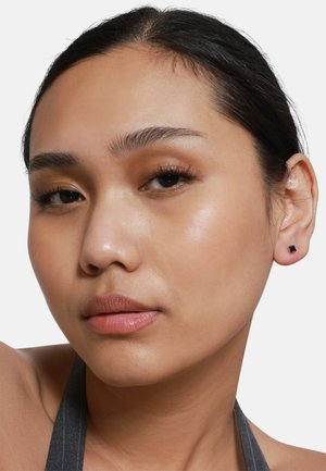 Boucles d'oreilles carrées noires en métal doré. Surface lisse, design minimaliste. Modèle avec un maquillage naturel, arrière-plan neutre.